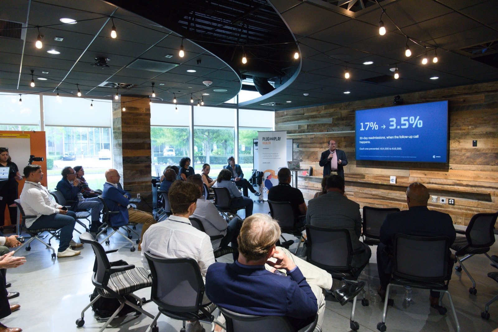 RJ Burnham presenting to a full room at the Plug and Play Health Innovation Lounge, beside a slide reading "17% to 3.5%".